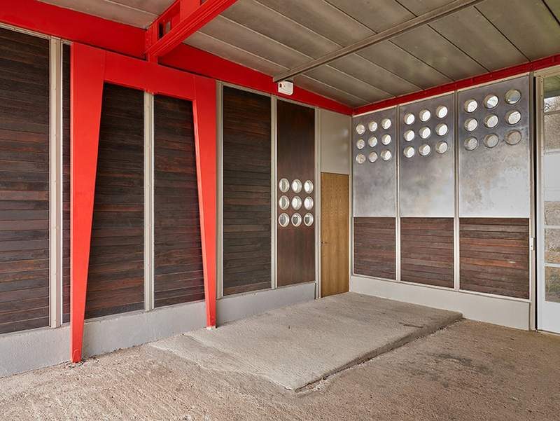 The corner of the covered play area: aluminium panels pierced with portholes, boarding and red strut