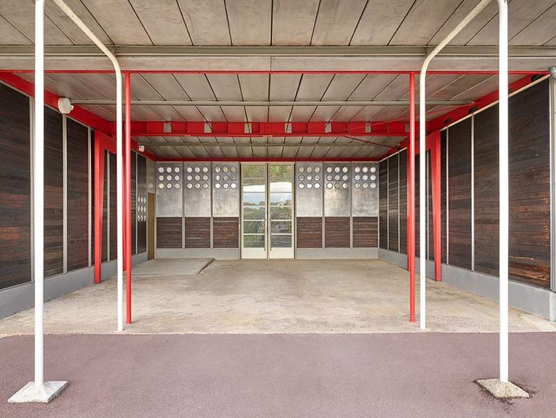 The covered play area on axis: red portal frames, portholes, the glazed door beyond